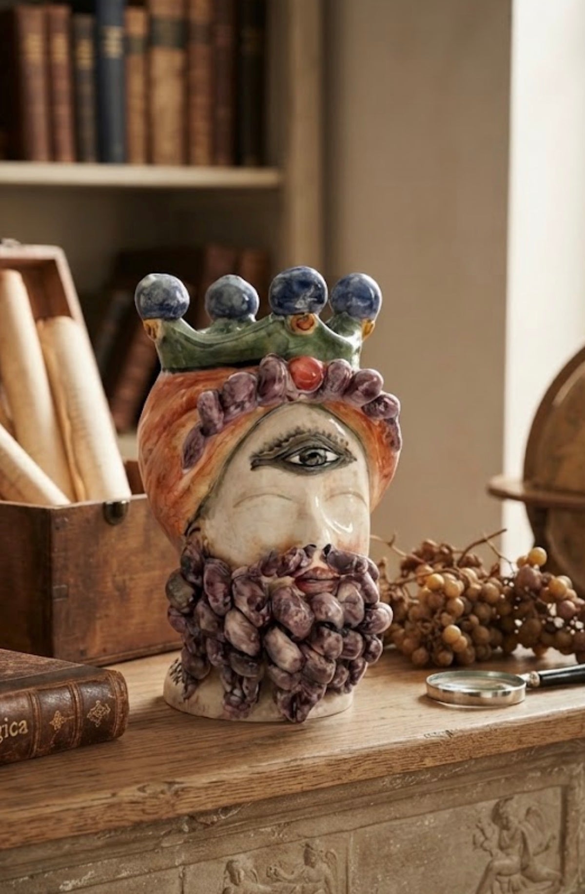 Testa di Polifemo Re in ceramica siciliana con corona verde e barba viola, ambientata su una consolle