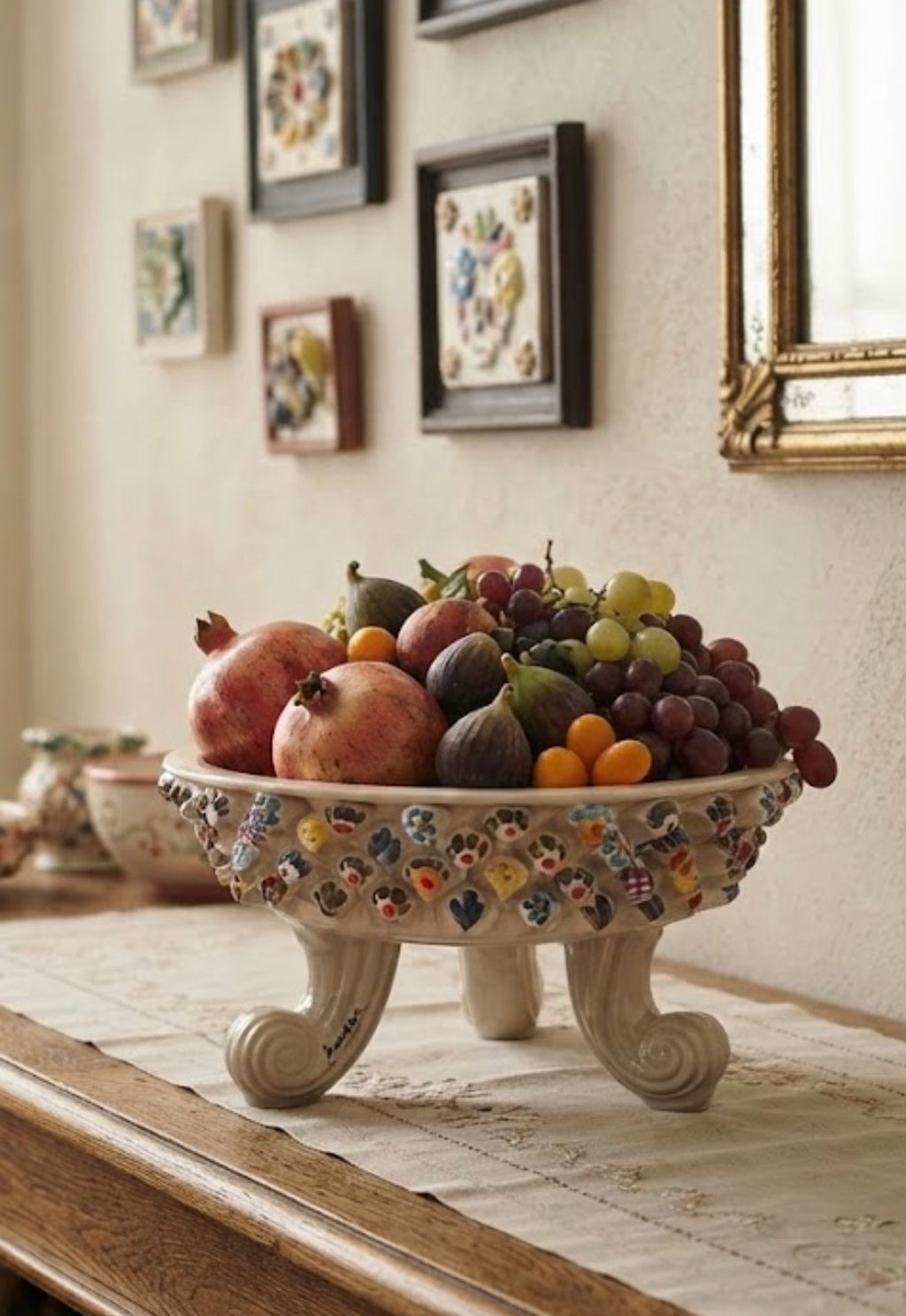 Centrotavola tripode Murry in ceramica avorio con decori colorati, ambientato su un tavolo con frutta