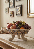 Centrotavola tripode Murry in ceramica avorio con decori colorati, ambientato su un tavolo con frutta