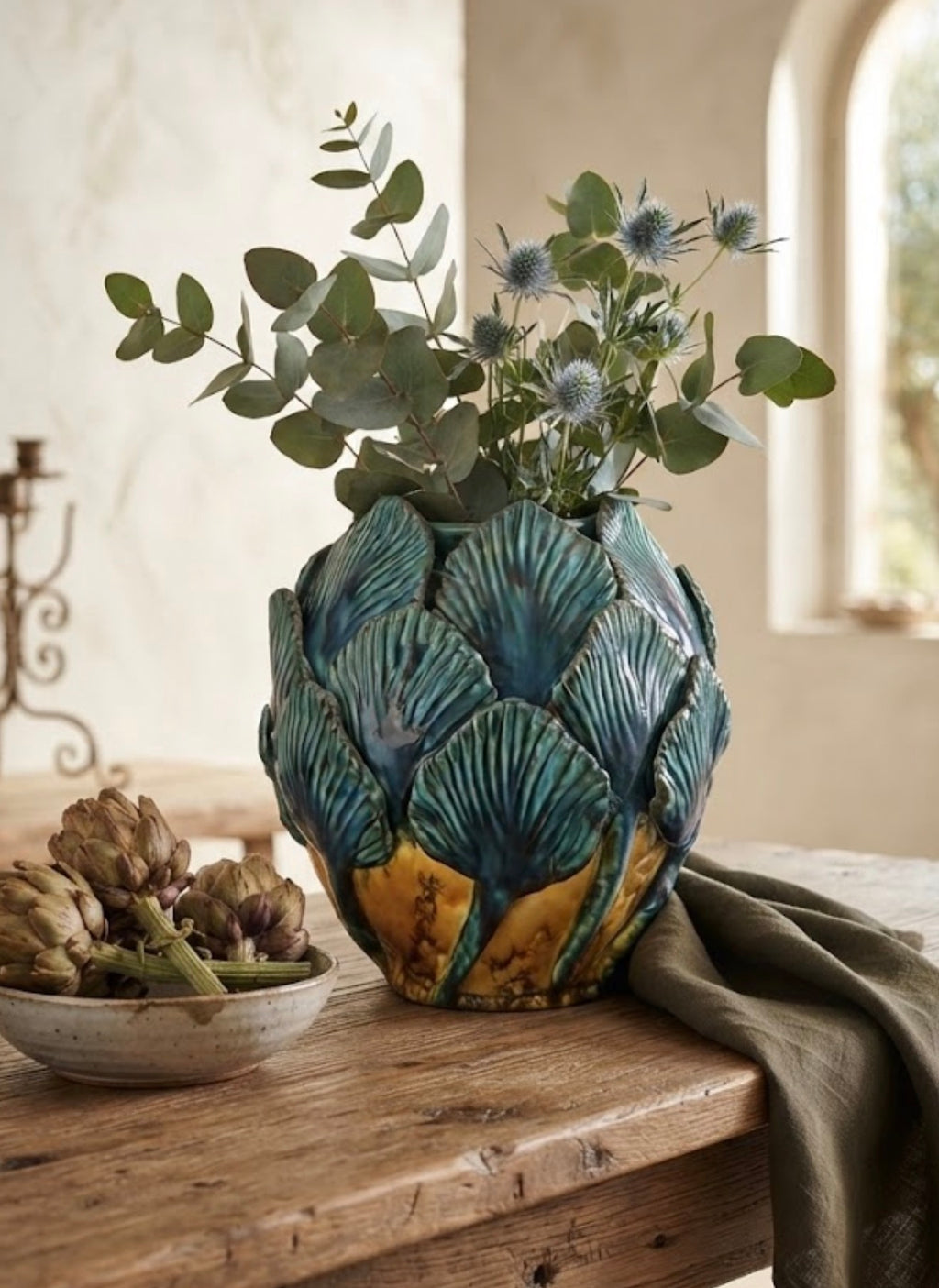 Vaso Bali verde petrolio e ocra con petali in rilievo, ambientato su un tavolo con rami decorativi